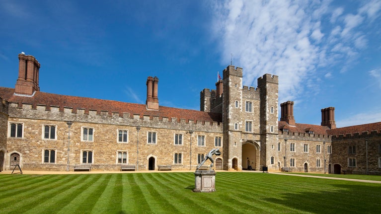 Large old, stone building with bright blue sky above and green grass in front.